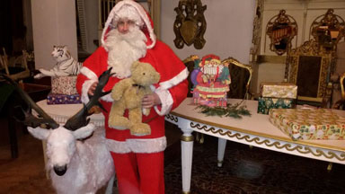 Der Weihnachtsmann steht nehmen seinem Rentier und hält einen Stoffbären in der Hand